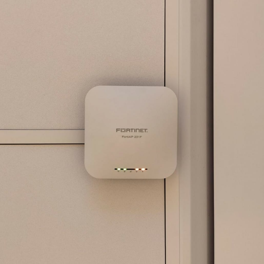 Fortinet FortiAP 231F monterad på väggen intill en dörrkarm på kontoret, med lysdioderna tända