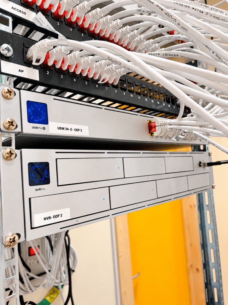 Nätverksskåp i skolan med patchpaneler märkta ACCESS och AP, en UniFi USW Pro 24-switch och en UniFi NVR Pro med vita nätverkskablar
